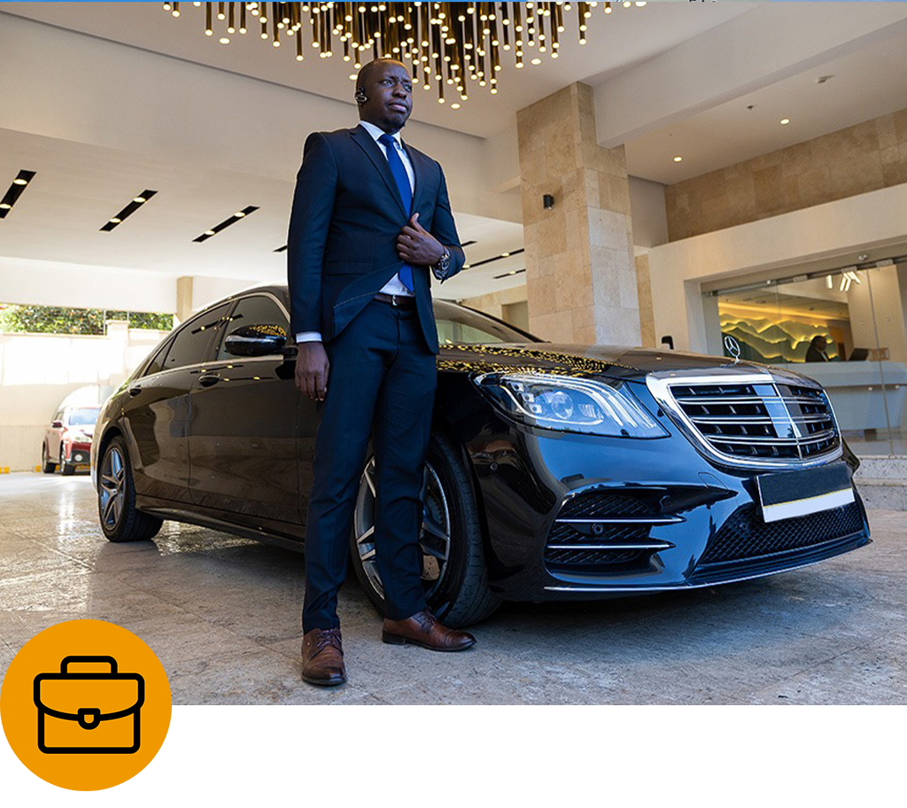 Comfleete corporate transport featuring a professional chauffeur beside a black Mercedes-Benz executive sedan at a hotel entrance, ready for business travel and executive transfers.